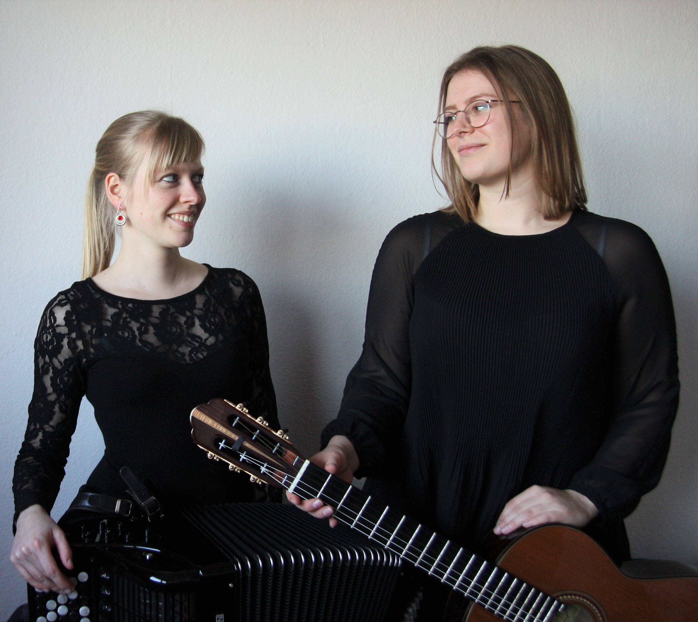 Die beiden Künstlerinnen des Duo Andromeda sitzen nebeneinander mit einem Akkordeon und einer Gitarre und schauen sich an