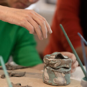Eine Frau bemalt ein selbstgetöpfertes Gefäß aus Keramik mit einem Pinsel